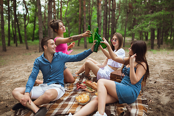 Image showing Group of friends clinking beer bottles during picnic in summer forest. Lifestyle, friendship