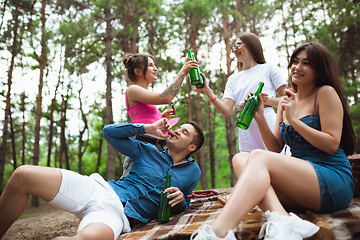 Image showing Group of friends clinking beer bottles during picnic in summer forest. Lifestyle, friendship