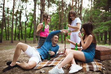 Image showing Group of friends clinking beer bottles during picnic in summer forest. Lifestyle, friendship