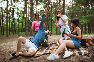 Image showing Group of friends clinking beer bottles during picnic in summer forest. Lifestyle, friendship