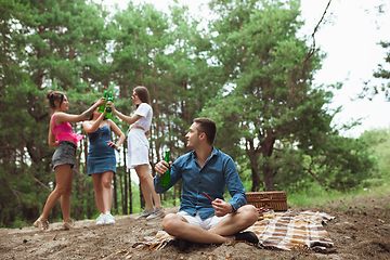 Image showing Group of friends clinking beer bottles during picnic in summer forest. Lifestyle, friendship