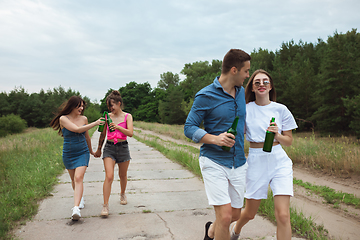 Image showing Group of friends clinking beer bottles during picnic in summer forest. Lifestyle, friendship