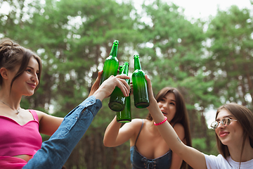 Image showing Group of friends clinking beer bottles during picnic in summer forest. Lifestyle, friendship