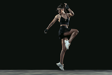 Image showing Beautiful young female athlete practicing on black studio background, full length portrait