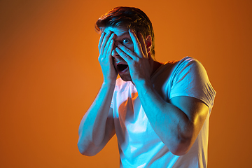 Image showing Caucasian beautiful young man\'s portrait on gradient orange studio background, emotional and expressive. Copyspace for ad.