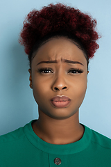 Image showing African-american beautiful young woman\'s close up portrait on blue studio background, emotional and expressive. Copyspace for ad.