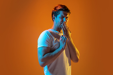 Image showing Caucasian beautiful young man\'s portrait on gradient orange studio background, emotional and expressive. Copyspace for ad.