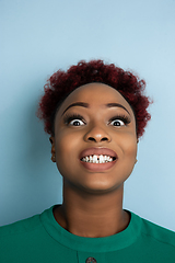 Image showing African-american beautiful young woman\'s close up portrait on blue studio background, emotional and expressive. Copyspace for ad.