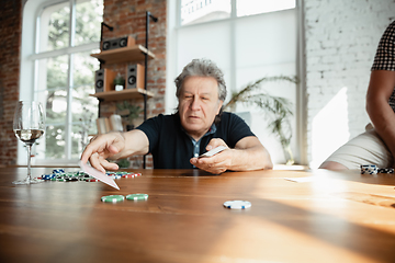 Image showing Senior man playing cards and drinking wine with friends, looks happy