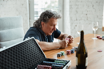 Image showing Senior man playing cards and drinking wine with friends, looks happy