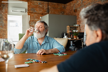 Image showing Two happy mature friends playing cards and drinking wine