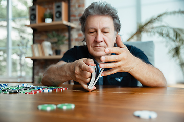 Image showing Senior man playing cards and drinking wine with friends, looks happy