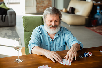 Image showing Senior man playing cards and drinking wine with friends, looks happy
