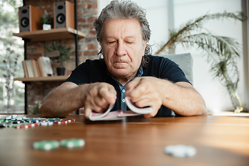 Image showing Senior man playing cards and drinking wine with friends, looks happy