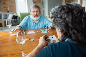 Image showing Two happy mature friends playing cards and drinking wine