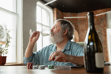 Image showing Senior man playing cards and drinking wine with friends, looks happy