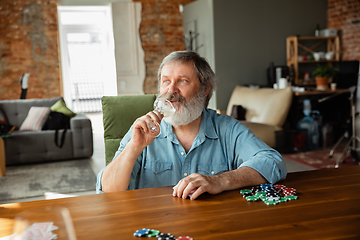 Image showing Senior man playing cards and drinking wine with friends, looks happy