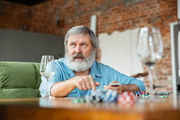 Image showing Senior man playing cards and drinking wine with friends, looks happy