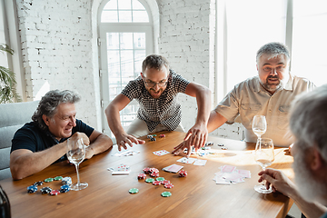 Image showing Group of happy mature friends playing cards and drinking wine