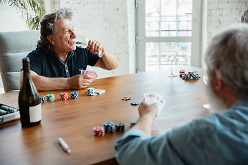 Image showing Two happy mature friends playing cards and drinking wine