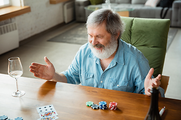 Image showing Senior man playing cards and drinking wine with friends, looks happy