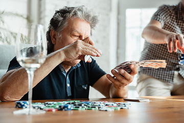 Image showing Two happy mature friends playing cards and drinking wine