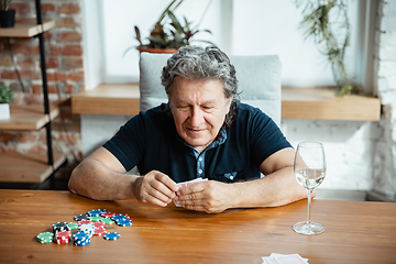 Image showing Senior man playing cards and drinking wine with friends, looks happy