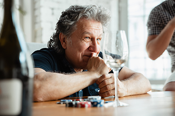 Image showing Senior man playing cards and drinking wine with friends, looks happy