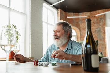 Image showing Senior man playing cards and drinking wine with friends, looks happy