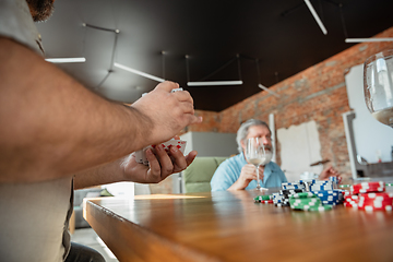 Image showing Two happy mature friends playing cards and drinking wine