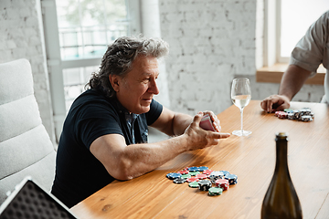 Image showing Senior man playing cards and drinking wine with friends, looks happy