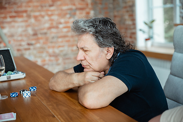 Image showing Senior man playing cards and drinking wine with friends, looks happy