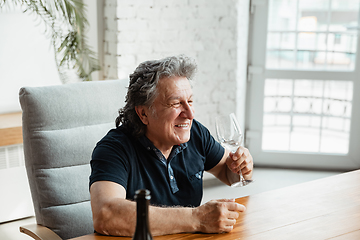 Image showing Senior man playing cards and drinking wine with friends, looks happy