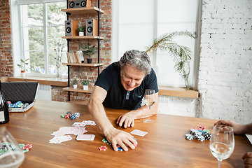 Image showing Senior man playing cards and drinking wine with friends, looks happy