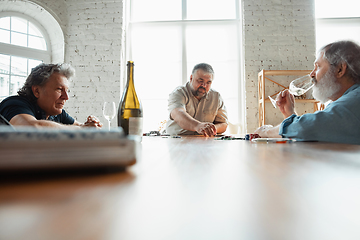 Image showing Group of happy mature friends playing cards and drinking wine