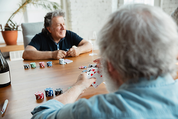 Image showing Two happy mature friends playing cards and drinking wine