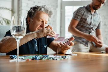 Image showing Two happy mature friends playing cards and drinking wine