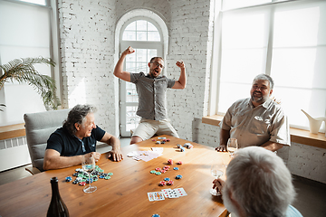 Image showing Group of happy mature friends playing cards and drinking wine