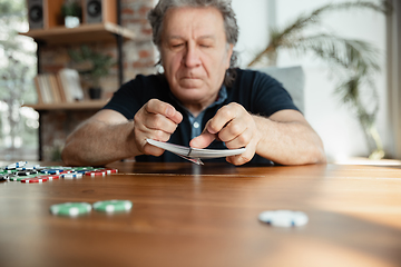 Image showing Senior man playing cards and drinking wine with friends, looks happy