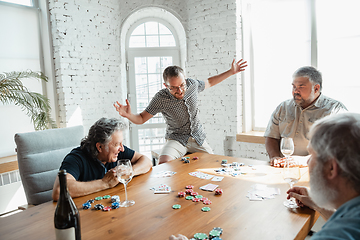 Image showing Group of happy mature friends playing cards and drinking wine