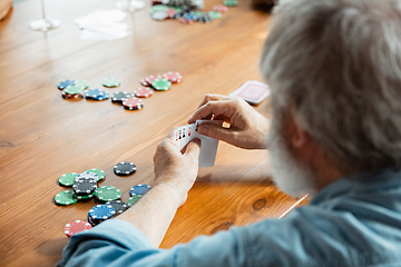 Image showing Senior man playing cards and drinking wine with friends, looks happy