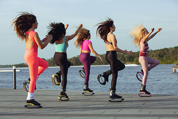 Image showing Beautiful women in sportswear jumping in a kangoo jumps shoes at the street on summer\'s sunny day