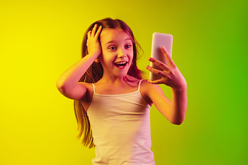 Image showing Little caucasian girl\'s portrait isolated on gradient background in neon light. Concept of human emotions, facial expression, modern gadgets and technologies. Copyspace.