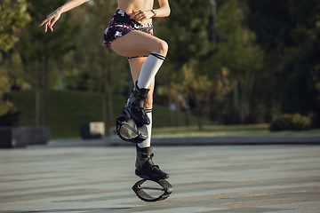 Image showing Beautiful woman in sportswear jumping in a kangoo jumps shoes at the street on summer\'s sunny day