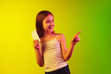 Image showing Little caucasian girl\'s portrait isolated on gradient background in neon light. Concept of human emotions, facial expression, modern gadgets and technologies. Copyspace.