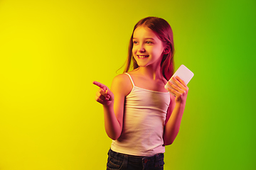 Image showing Little caucasian girl\'s portrait isolated on gradient background in neon light. Concept of human emotions, facial expression, modern gadgets and technologies. Copyspace.