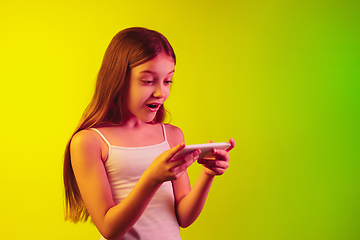 Image showing Little caucasian girl\'s portrait isolated on gradient background in neon light. Concept of human emotions, facial expression, modern gadgets and technologies. Copyspace.