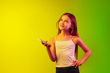 Image showing Little caucasian girl\'s portrait isolated on gradient background in neon light. Concept of human emotions, facial expression, modern gadgets and technologies. Copyspace.