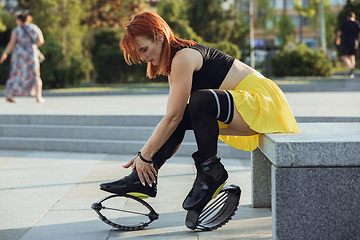 Image showing Beautiful woman in sportswear jumping in a kangoo jumps shoes at the street on summer\'s sunny day