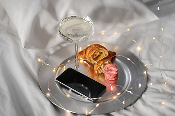 Image showing champagne glass, croissants and smartphone in bed